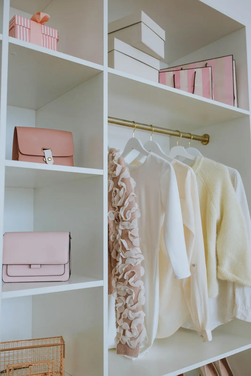 An organized white closet with hanging clothes, boxes and shoes