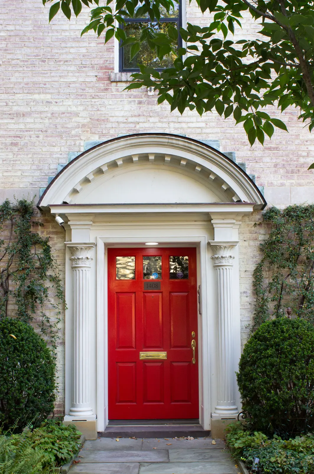 A red front door in a white doorway with boxwood shrubs