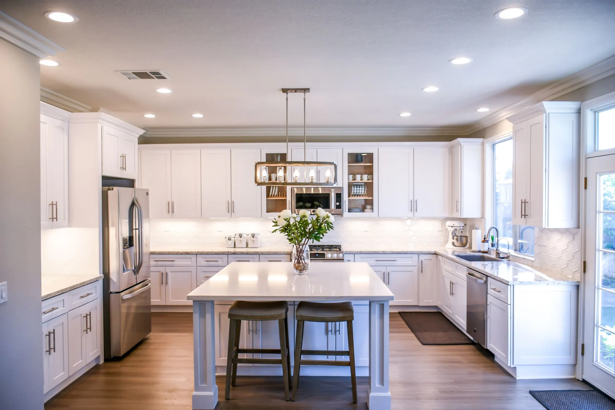 A bright, spotless white kitchen with an island, pendant light and a vase of white flowers