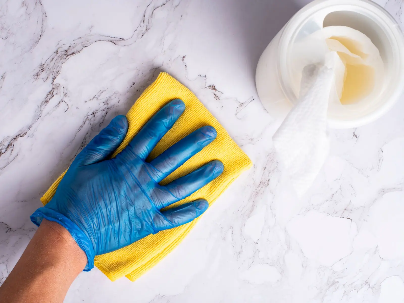 A gloved hand wiping a marble countertop with a sponge