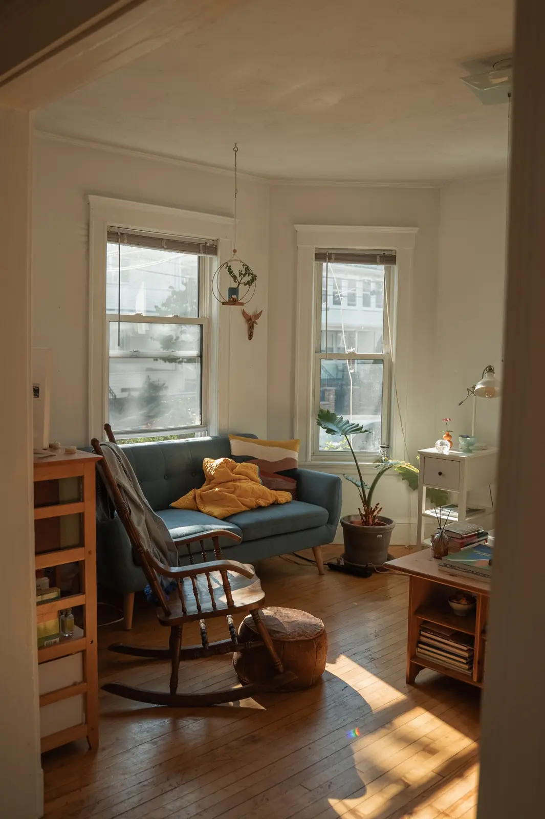 A sunlit living room with a bay window, wood floors and a rocking chair